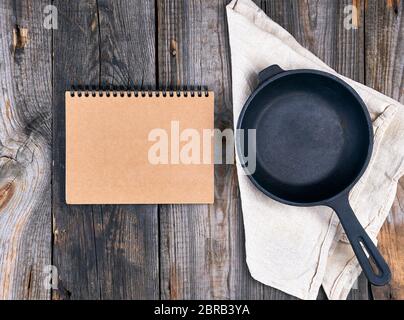 empty black round frying pan with handle and paper notebook on a wooden table, top view Stock Photo