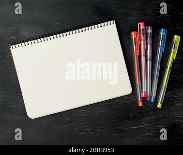 open notebook and gel pen on a black wooden background, top view, empty white sheets Stock Photo