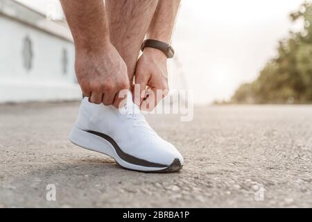 portrait of Caucasian guy in a blue t-shirt and black shorts,who ties his laces on white sports shoes before Jogging Stock Photo