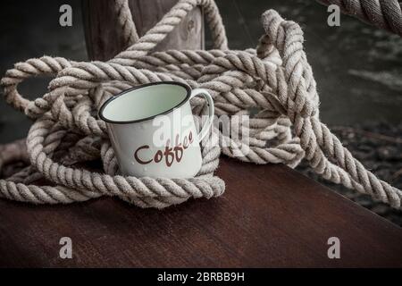 https://l450v.alamy.com/450v/2brbb9h/rustic-enamel-coffee-cup-with-word-coffee-on-it-and-decorative-thick-rope-on-a-wooden-jetty-at-the-waters-edge-2brbb9h.jpg