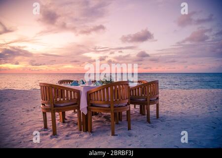Sunset moody beach landscape in luxury resort, beach dinner. Decorated table with dinner set up on the tropical beach. Stock Photo