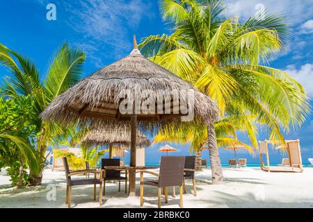 Cafe on the beach, ocean and sky as tropical landscape. Chairs with table under palm parasol. Exotic summer outdoor restaurant family vacation concept Stock Photo