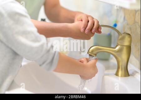 Mother teaching son sanitary prevention measures washing hands in pandemic crisis Stock Photo