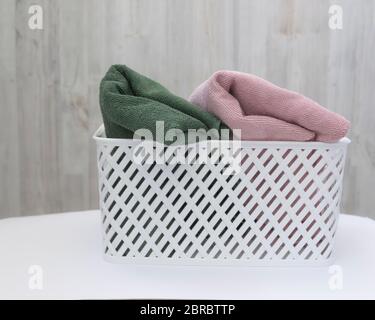 White plastic basket with clean multi-colored towels on a wall background Stock Photo