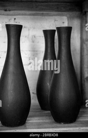 Three empty black ceramic vases on wooden shelf against concrete wall. Total black concept. Stock Photo
