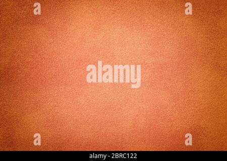 Orange matte background of suede fabric, closeup. Velvet texture of seamless coral leather. Felt material macro with dark vignette. Stock Photo