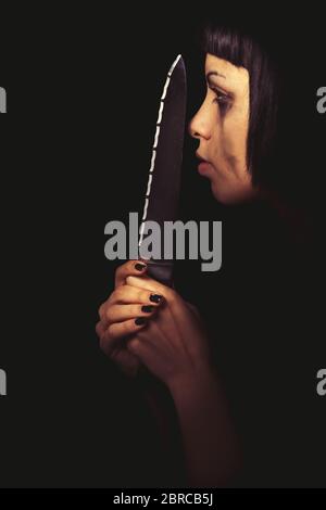 Killer profile. Murderous woman. Domestic crime. The profile of a young woman with a knife in her hand. In the darkness her face is illuminated. Cryin Stock Photo