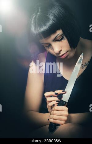 Murderous suicide girl with knife. Crime concept. A beautiful girl with a knife in hand has just committed a crime. Touching the blade watching the kn Stock Photo