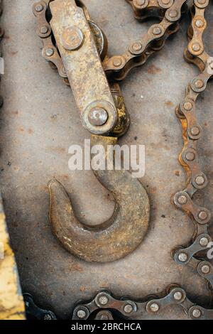 Old rusty soviet homemade winch, with traces of yellow paint. Hook, bicycle chain, chain links. The winch lies on a sheet of rusty iron. Scrap metal. Stock Photo