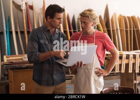 Two Caucasian male surfboard makers working on projects and using a laptop computer Stock Photo