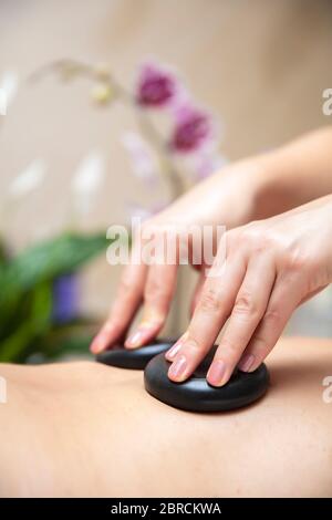 Massage therapist using hot lava stones on a beck of young woman during health spa relaxing stone therapy Stock Photo