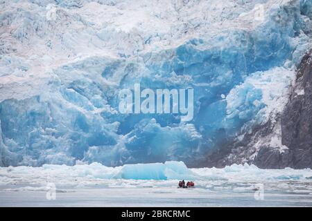 Tourists on a skiff boat get a close up scenic view of icebergs calved from South Sawyer Glacier, floating down Tracy Arm Fjord, Southeast Alaska, USA