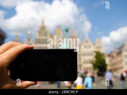 Antwerp, Flanders, Belgium. August 2019. In the town hall square, a smartphone frames the magnificent Renaissance buildings: the display is black and Stock Photo