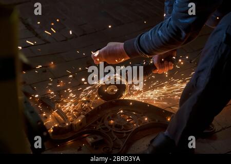 Side view of a man's hands working on a metal part of a garden bench, using an electric grinder while sparks are flying around in the industrial works Stock Photo