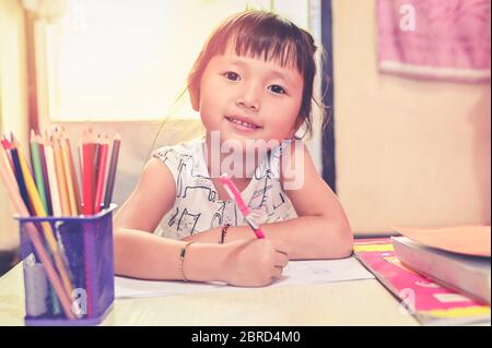 Little School girl looking camera or watching television screen for learning online sitting on floor in home online course for quarantine coronavirus Stock Photo