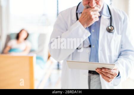 Unrecognizable senior male doctor standing in hospital room, using tablet. Stock Photo