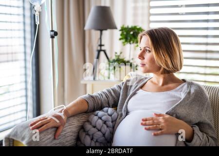 A portrait of pregnant woman with IV drip indoors at home or in hospital. Stock Photo