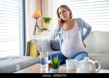 Portrait of pregnant woman in pain indoors at home, making phone call. Stock Photo