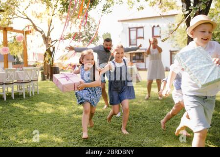 Small children ruunning with present outdoors in garden on birthday party. Stock Photo
