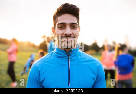 A portrait of young man with large group of people doing exercise in nature. Stock Photo