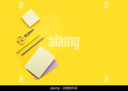 Different stationery on the yellow background notebooks, pencils and yellow stickers with the yellow and metallic scissors Stock Photo
