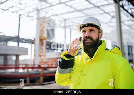 Man engineer standing on construction site, using smartphone. Stock Photo