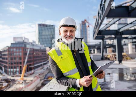 Man engineer standing outdoors on construction site, looking at camera. Stock Photo