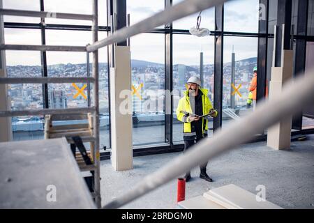 Man engineer standing on construction site, holding blueprints. Stock Photo