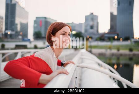Side view of young woman runner with earphones in city, stretching. Stock Photo
