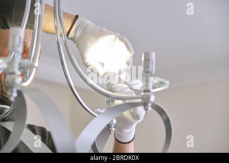 Installation ceiling lamp, hands of electrician fixing chandelier Stock Photo
