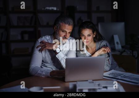 Architects with laptop sitting at the desk indoors in office, working late. Stock Photo