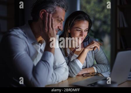 Architects with laptop sitting at the desk indoors in office, working late. Stock Photo