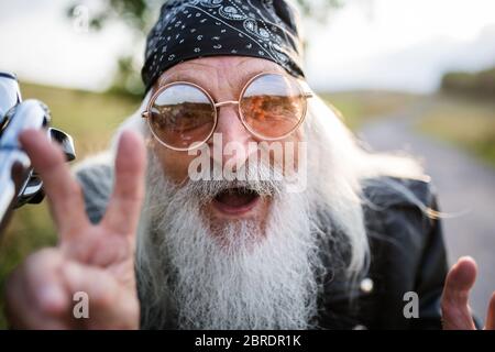 Close-up of senior man traveller with motorbike in countryside, having fun. Stock Photo