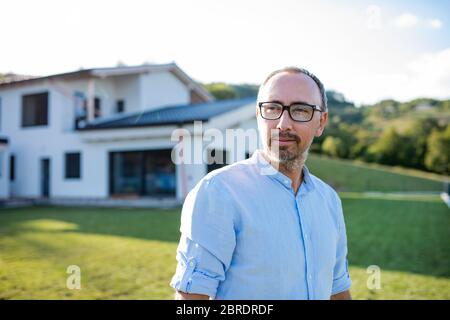 A portrait of man standing outdoors in garden by a house. Stock Photo
