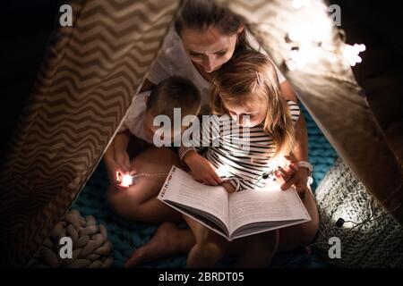 Mother with children sitting indoors in bedroom, reading a book. Stock Photo