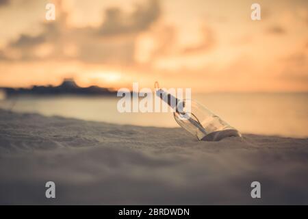 Message in the bottle washed ashore against the sun setting down. Tropical sunset beach design background. Castaway, loneliness, lost concept Stock Photo