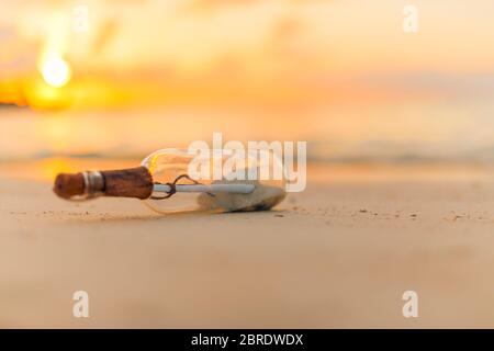Message in the bottle washed ashore against the sun setting down. Tropical sunset beach design background. Castaway, loneliness, lost concept Stock Photo