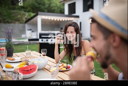Portrait of family with wine sitting at table outdoors on garden barbecue. Stock Photo