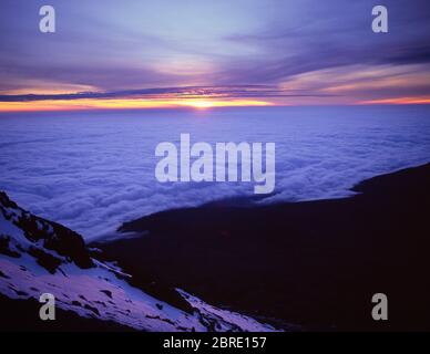 Tanzania, East Africa. Sunrise over Kenya from the Kibo summit slopes of Mount Kilimanjaro at Gillmans Point with cloud cover on the plains far below. Stock Photo