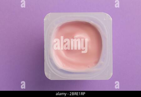 Healthy strawberry fruit flavored yoghurt with natural coloring in small plastic cup isolated on purple background  - overhead photo Stock Photo