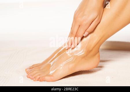 a young woman applies lotion to her feet on white towel Stock Photo
