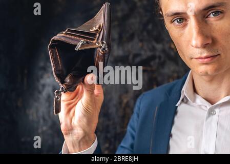 The man is holding an open empty brown leather wallet purse. The concept of economic crisis and business bankruptcy in the post-pandemic period Stock Photo