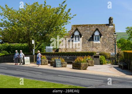 Exterior of quaint attractive cottage tea rooms cafe in scenic rural village (3 women waiting by bus stop) - Bolton Abbey, Yorkshire Dales, England UK Stock Photo