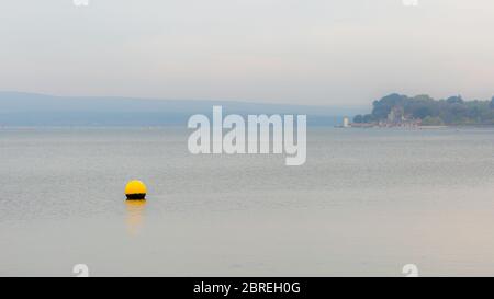Landscape photograph overlooking part of Poole Harbour with yellow shallow water buoy in foreground and Brownsea island in background on foggy day. Stock Photo