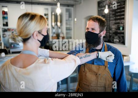 Coffee shop owners with face masks elbow bumping, open after lockdown quarantine. Stock Photo