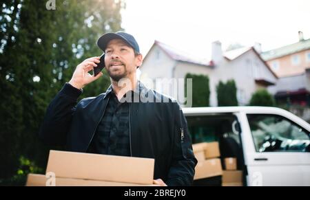 Delivery man courier delivering parcel box in town using smartphone. Stock Photo
