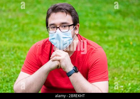 Fat man wearing face mask sitting on the grass Stock Photo