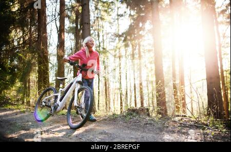 Active senior woman with e-bike cycling outdoors in nature. Stock Photo