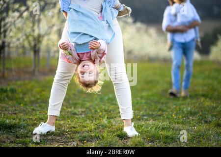 Unrecognizable mother holding small daughter upside down outdoors in spring nature. Stock Photo