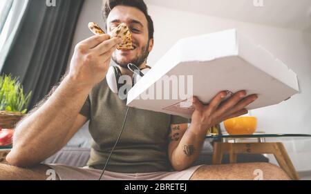 Young man eating pizza delivery at home - Happy guy having meal while playing video games in living room - Food and youth people entertainment concept Stock Photo